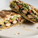 Close-up of a chicken crunch wrap with seasoned chicken, black beans, lettuce, avocado, tomato, and cheese
